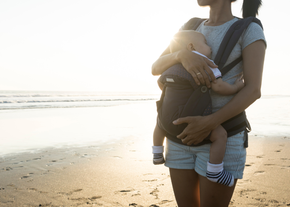 A mother on the beach with a baby in a carrier.