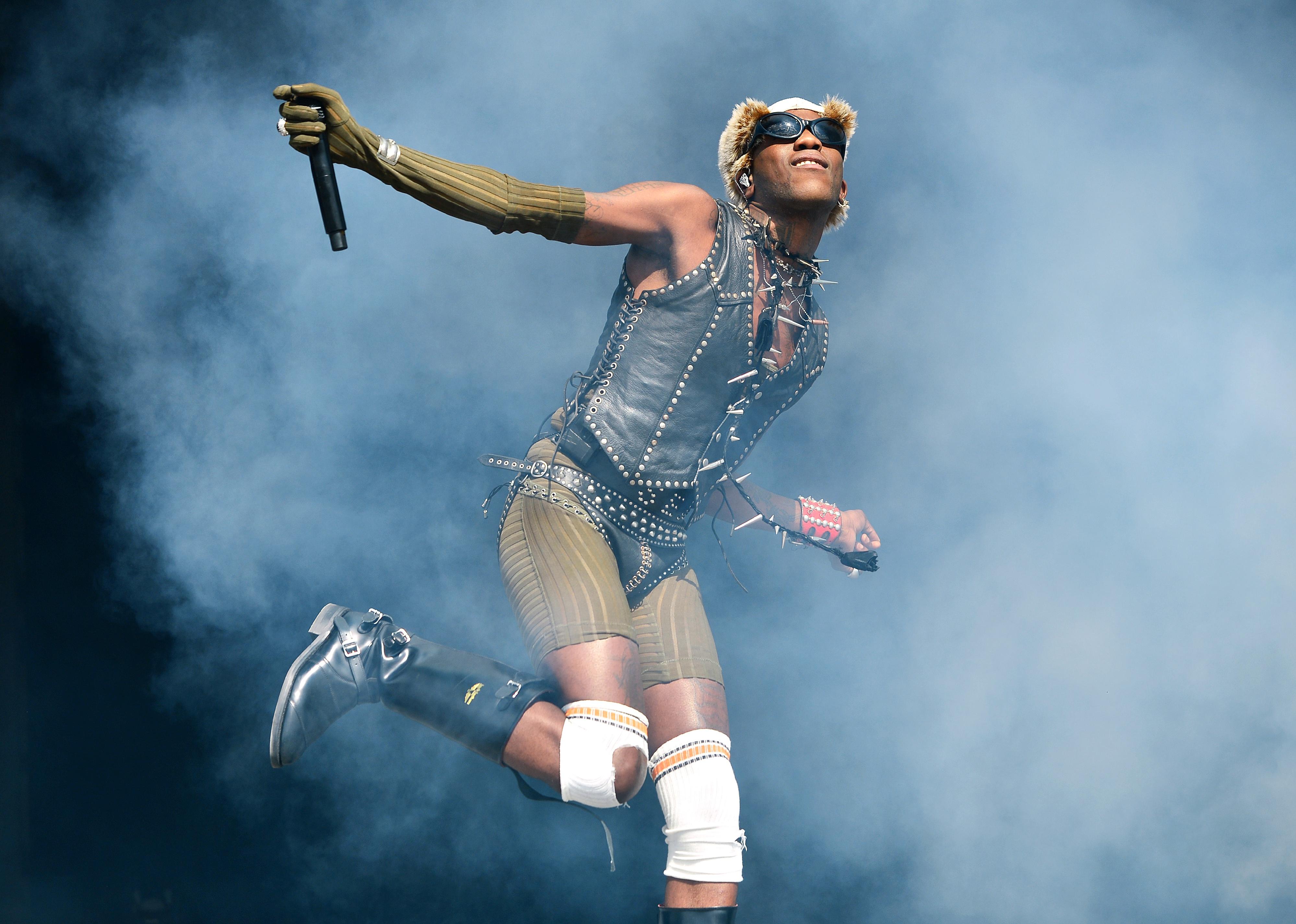 Yves Tumor performing in smoke in a leather vest and boots.