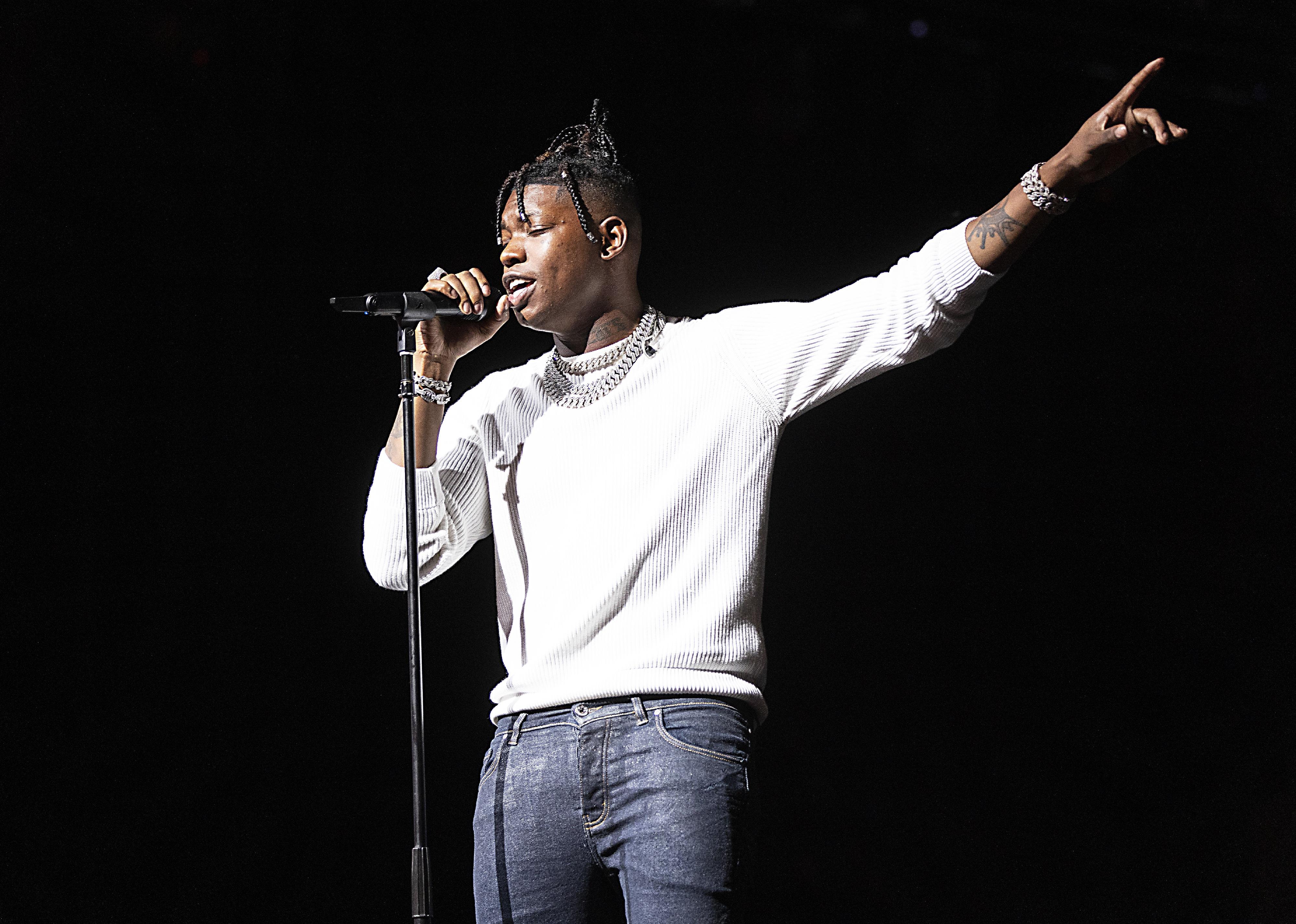 Yung Bleu performing onstage in jeans and a white sweater.