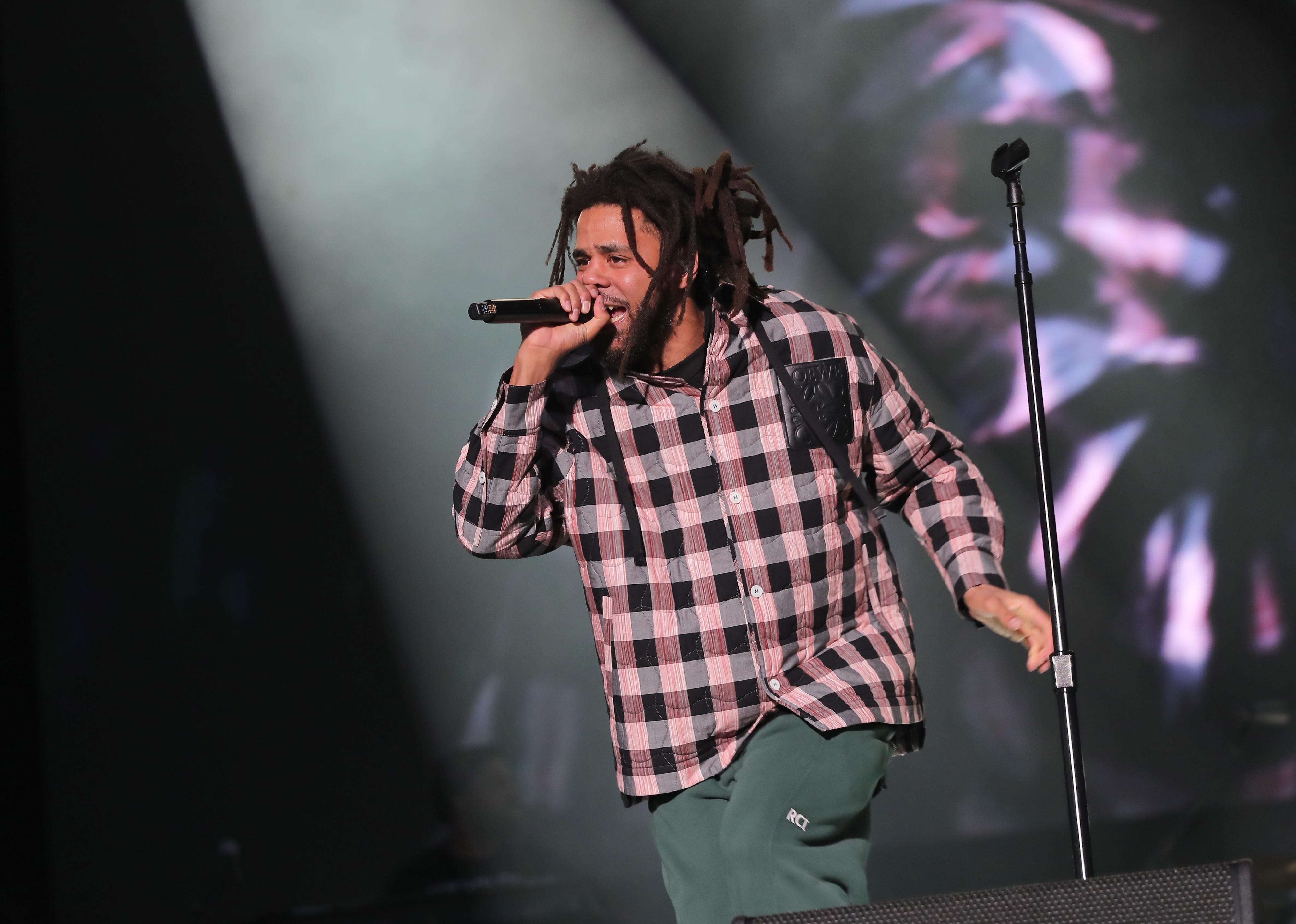 J. Cole performing onstage in a pink and black checkered shirt.