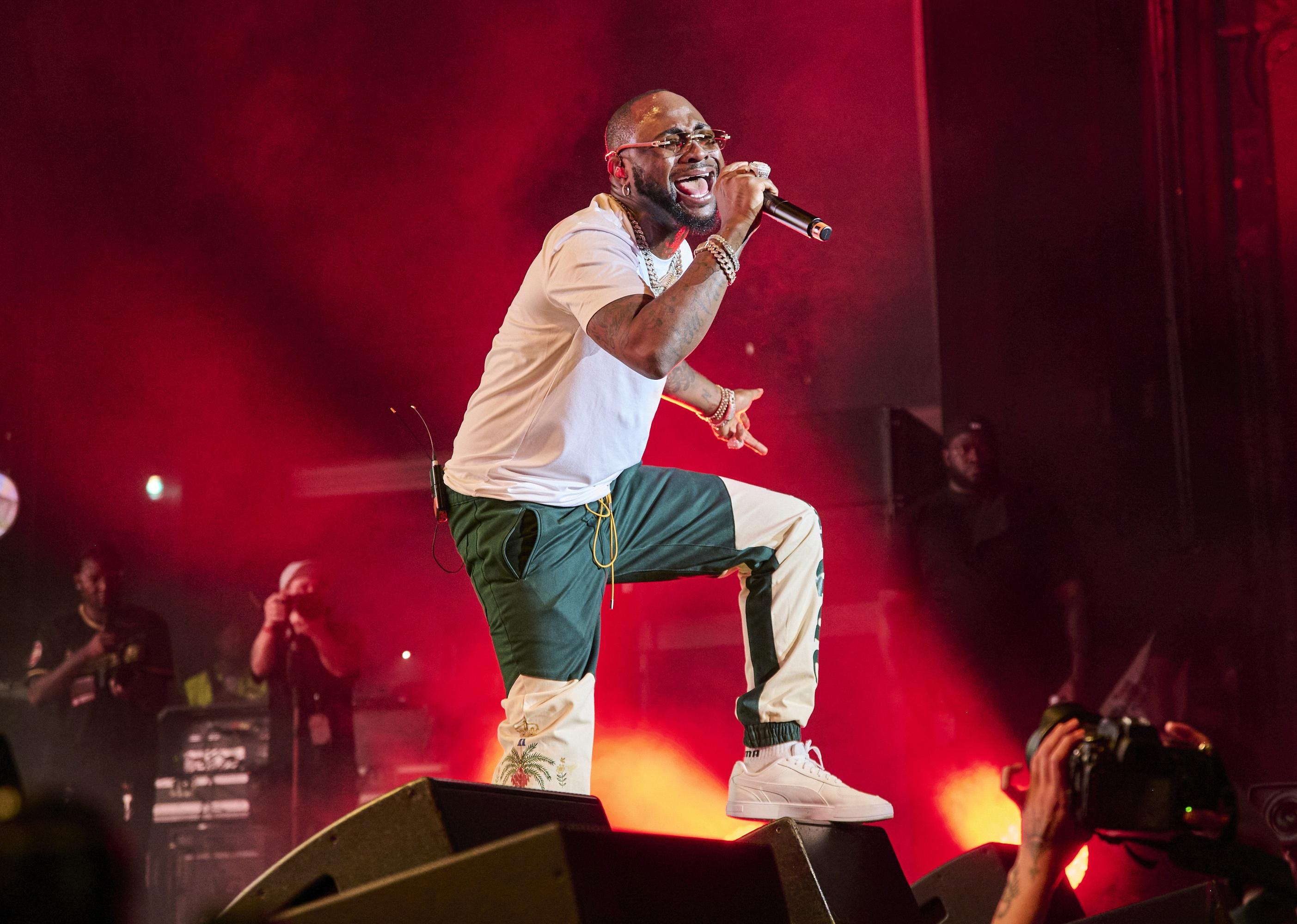 Davido dancing and singing onstage in green and white pants.