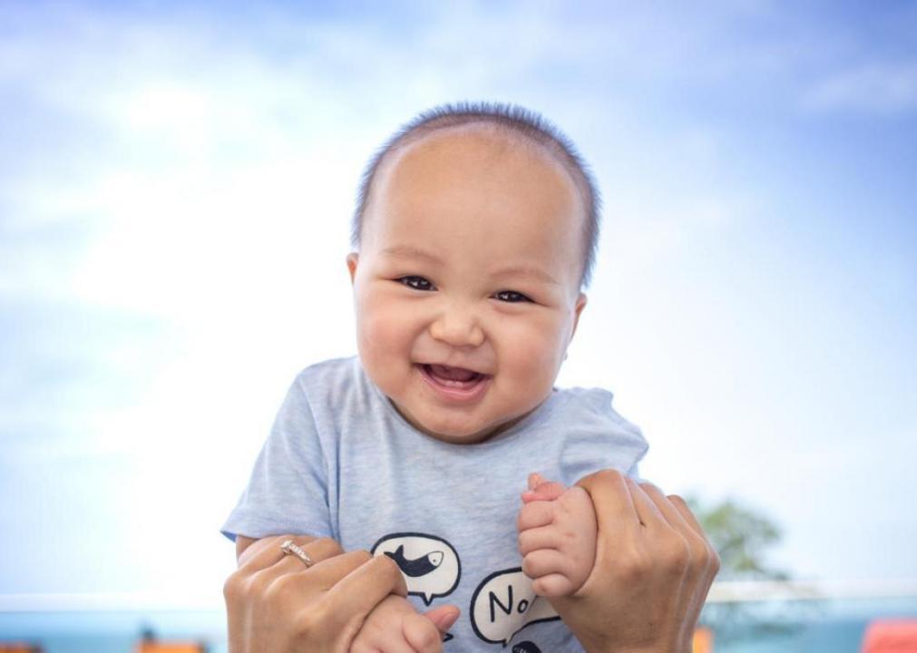 Smiling baby held in air wearing blue.