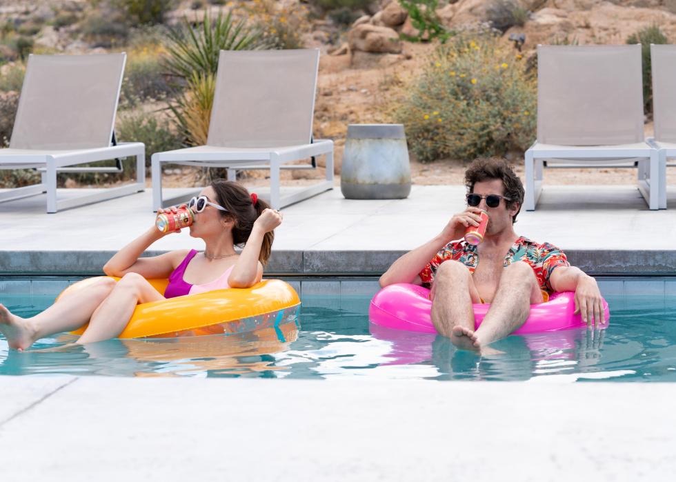 A man and woman float on tubes in a pool while drinking.