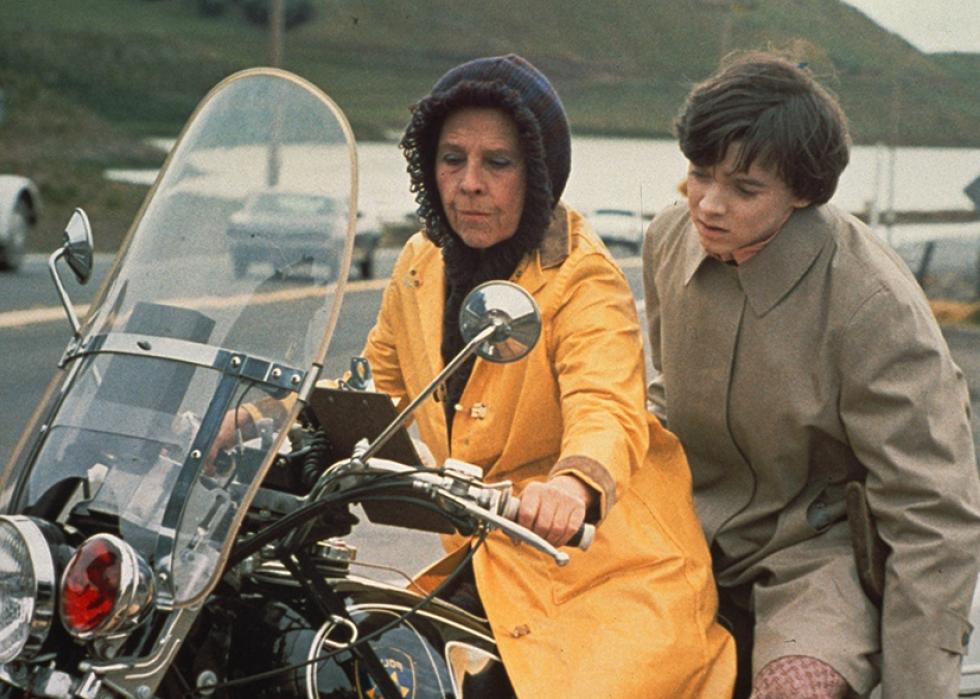 A woman in a yellow raincoat rides a motorcycle with a boy on the back.