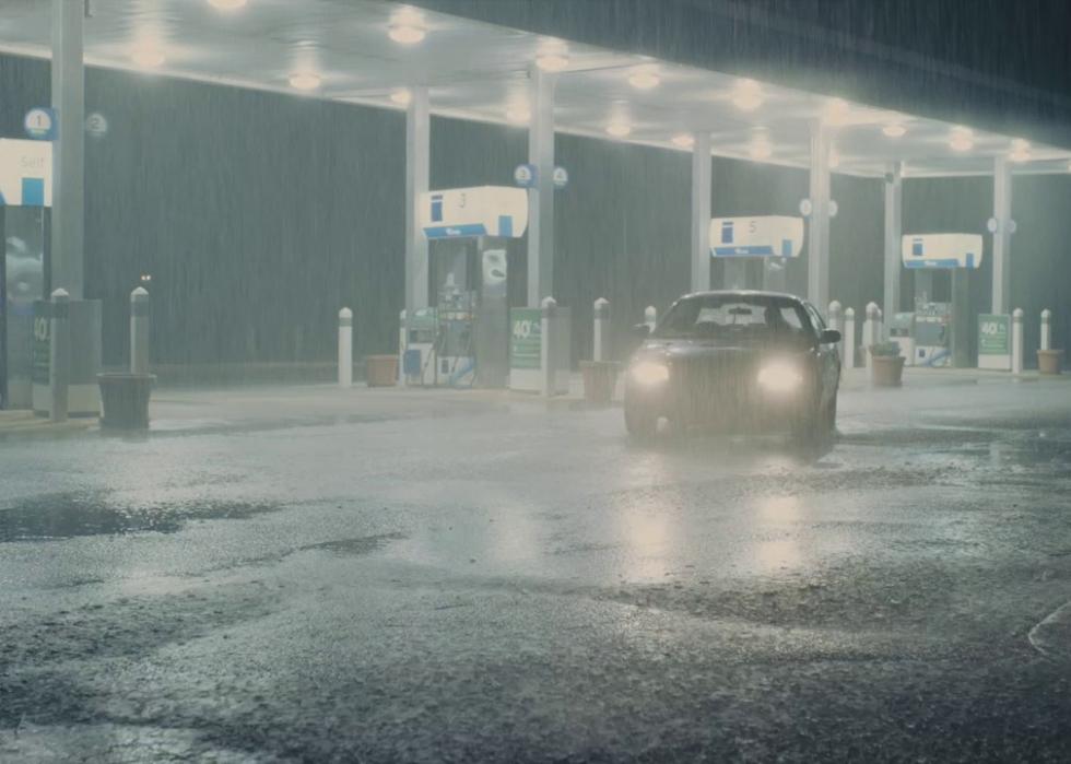 A car at a gas station in the pouring rain at night.