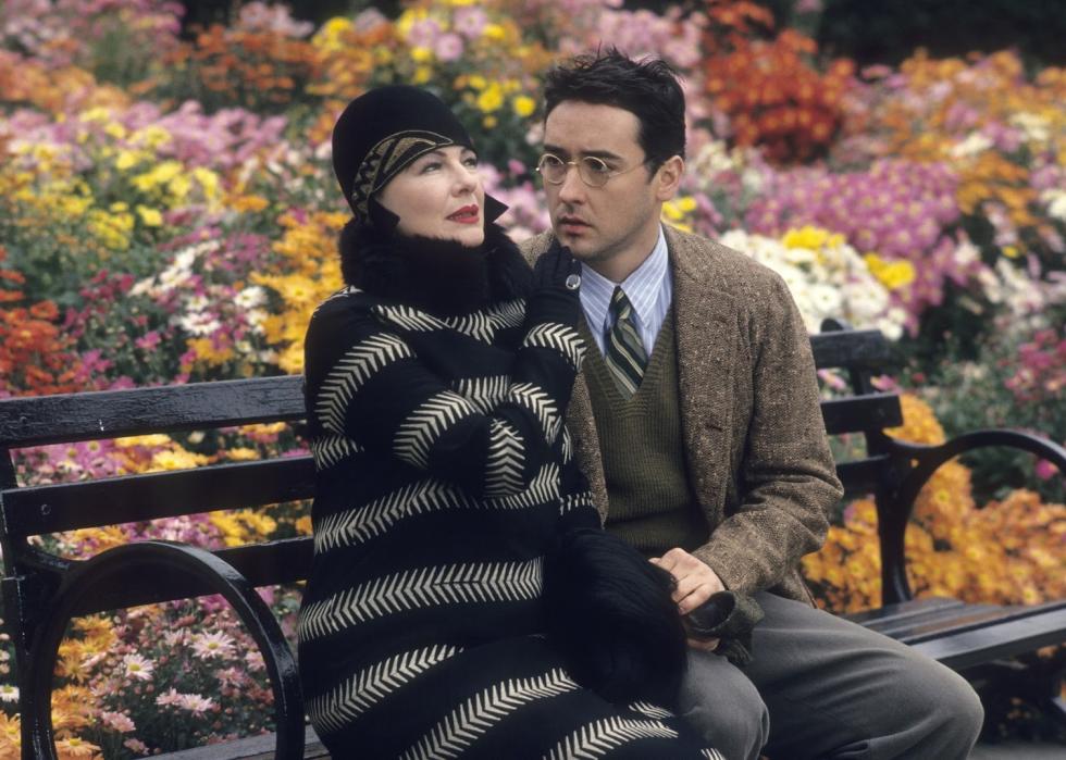 John Cusack and Dianne Wiest sit on a park bench surrounded by blooming flowers.
