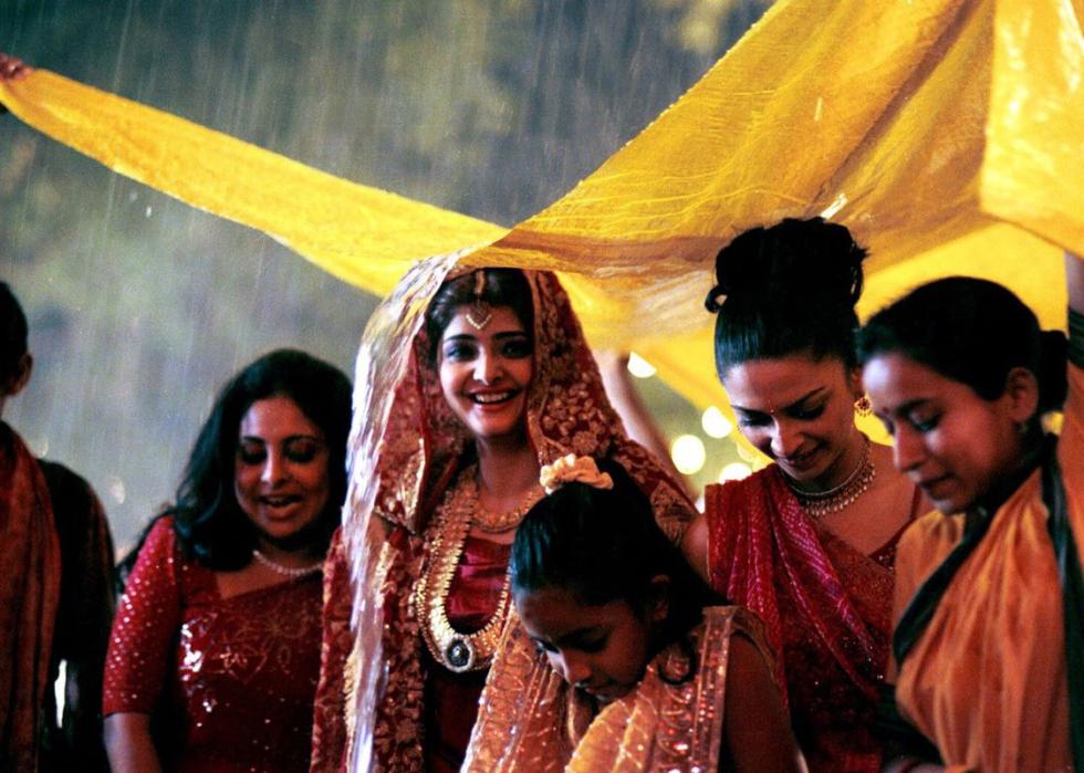 A group of happy people dressed for a traditional Indian marriage take cover from the rain.