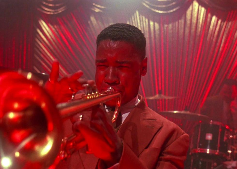 Denzel Washington playing the trumpet under a red light.