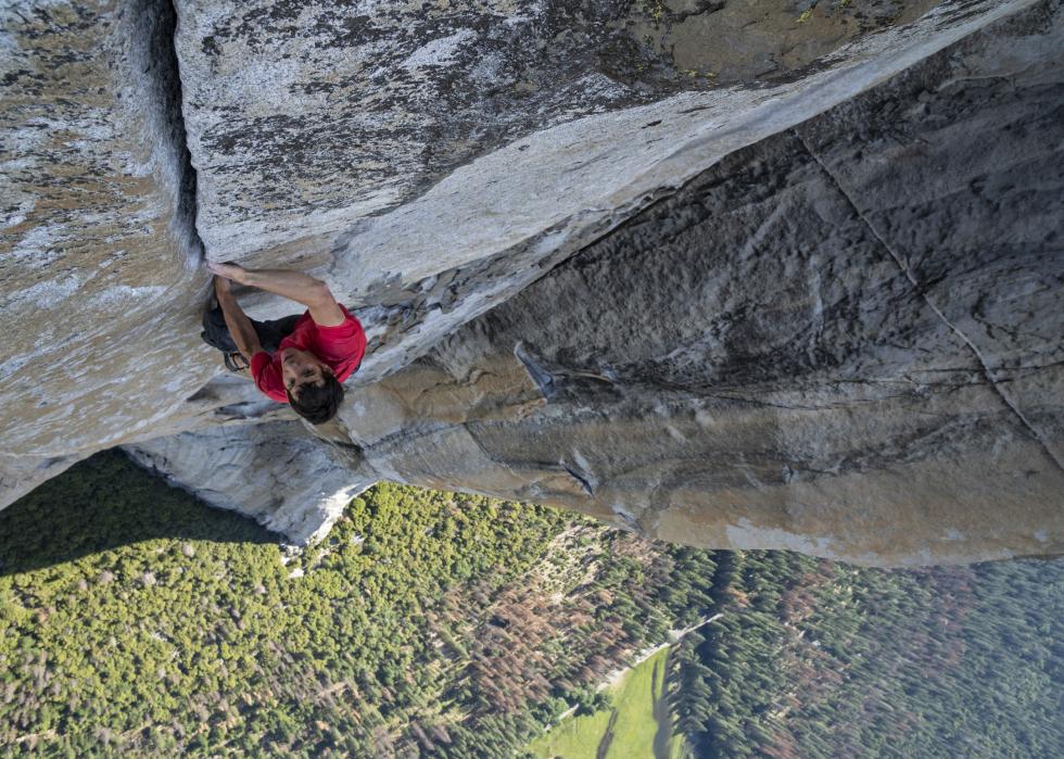 A man in a red shirt free climbing a monolith.