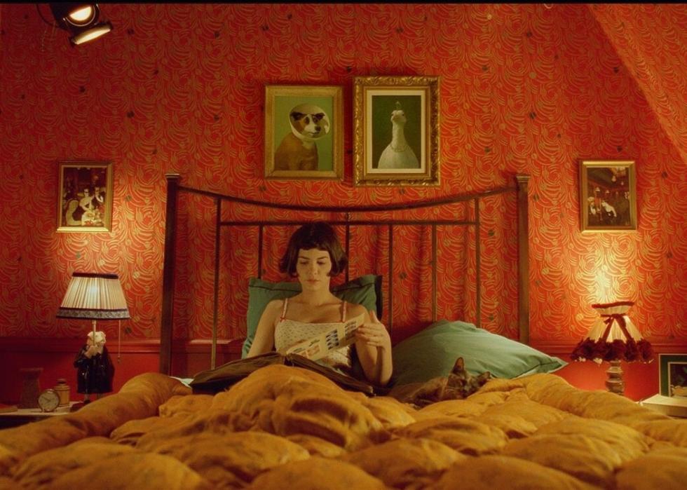 Audrey Tautou sitting in a bed looking at an album in front of a red wall.