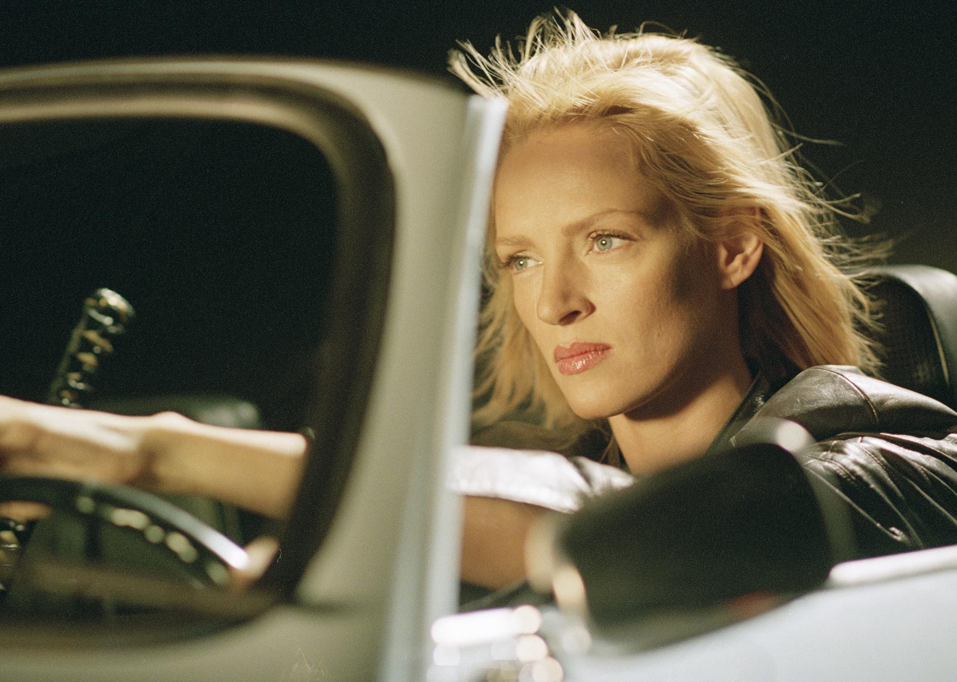 Uma Thurman driving a classic convertible with her hair blowing in the wind.
