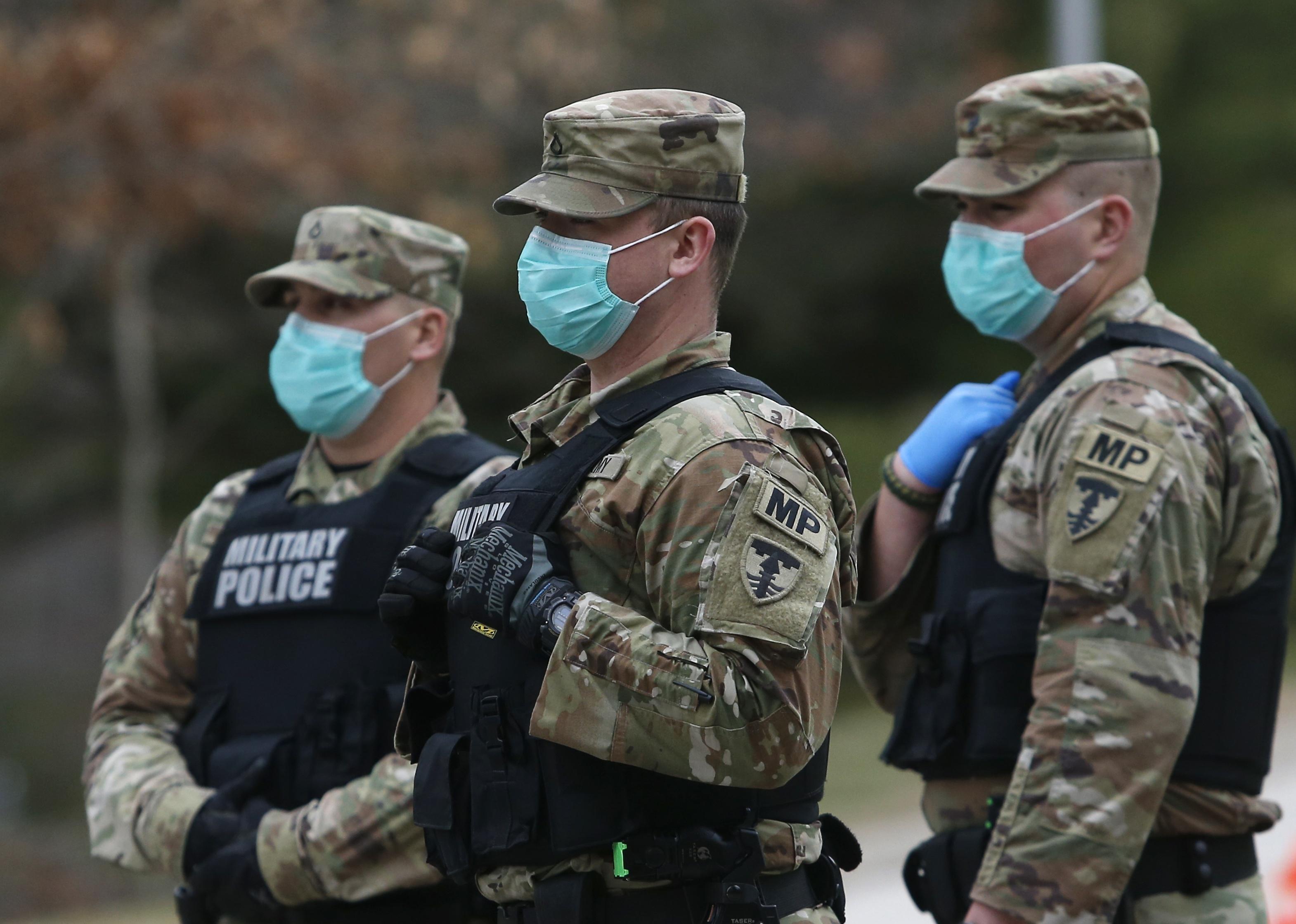 Military police wearing masks and gloves waiting at a checkpoint.