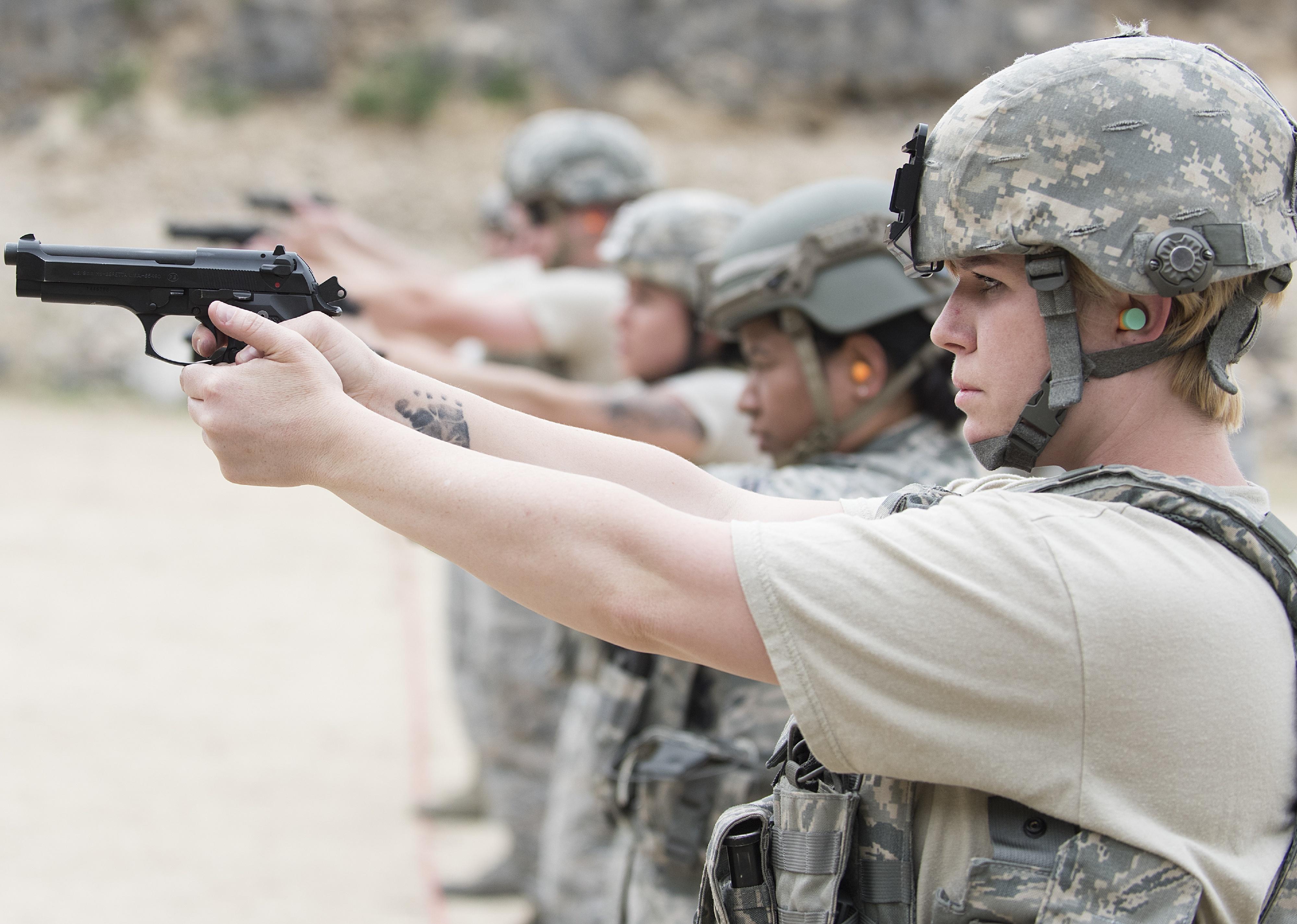 A line of women in camouflage and helmets aiming guns.