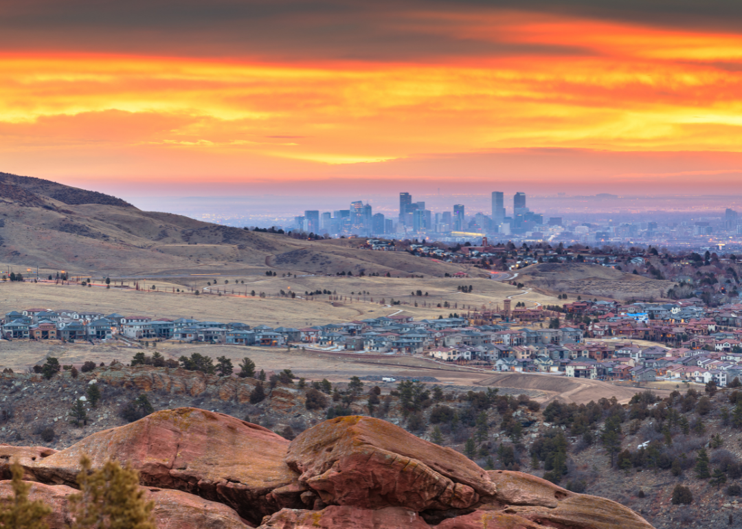 A faraway view of the skyline of Denver with homes in the foreground at sunset.