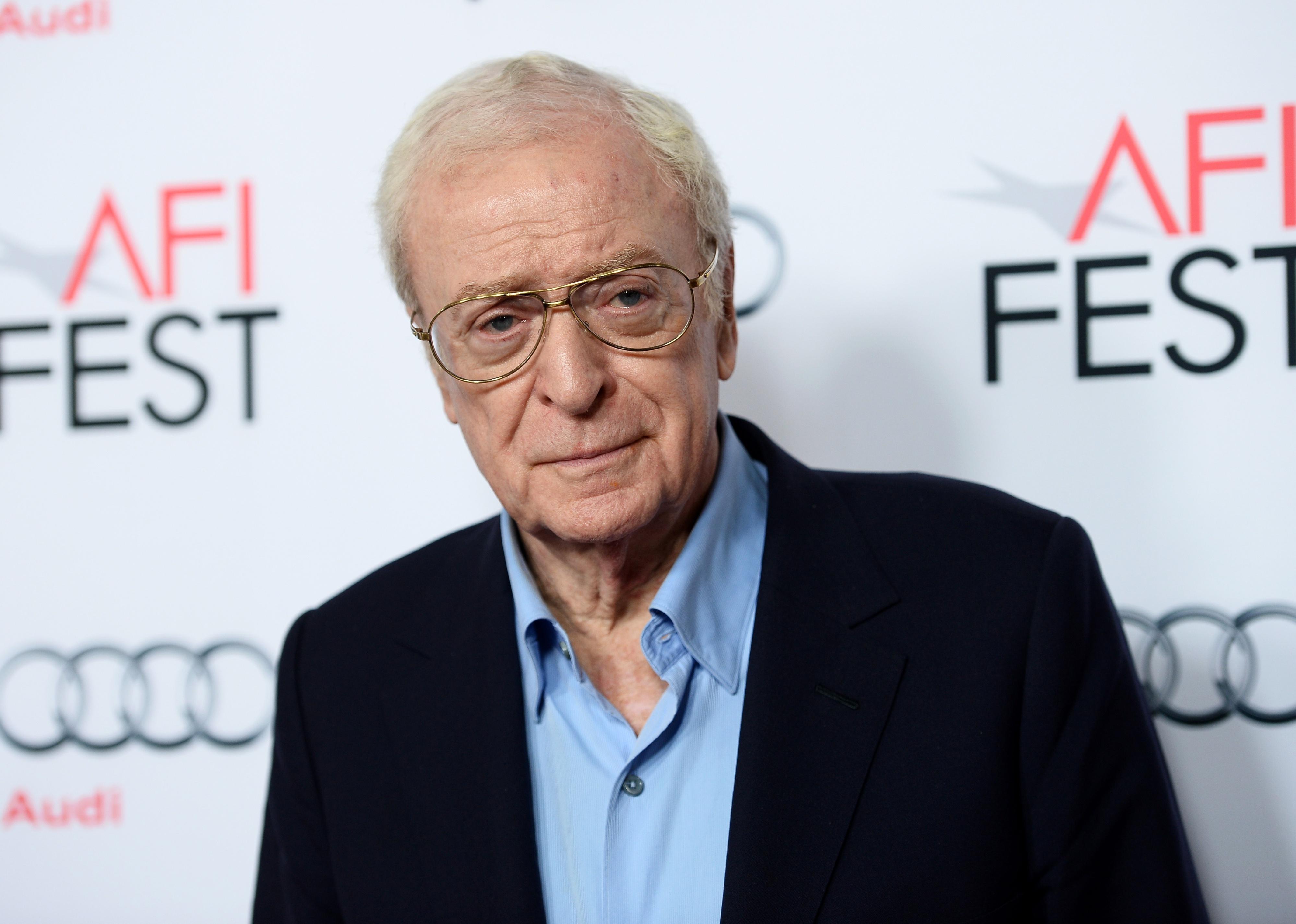 Michael Caine in a blue shirt and black jacket.