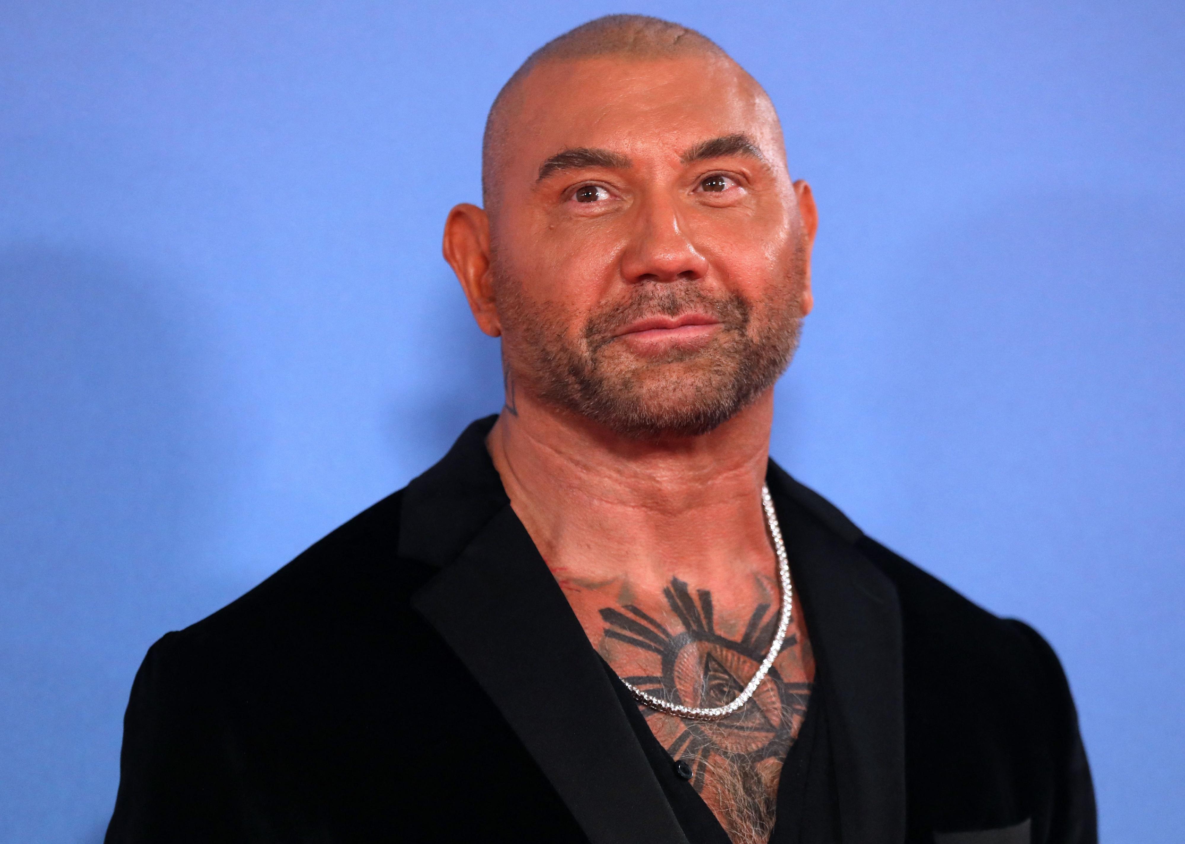 Dave Bautista in a black jacket against a blue background.