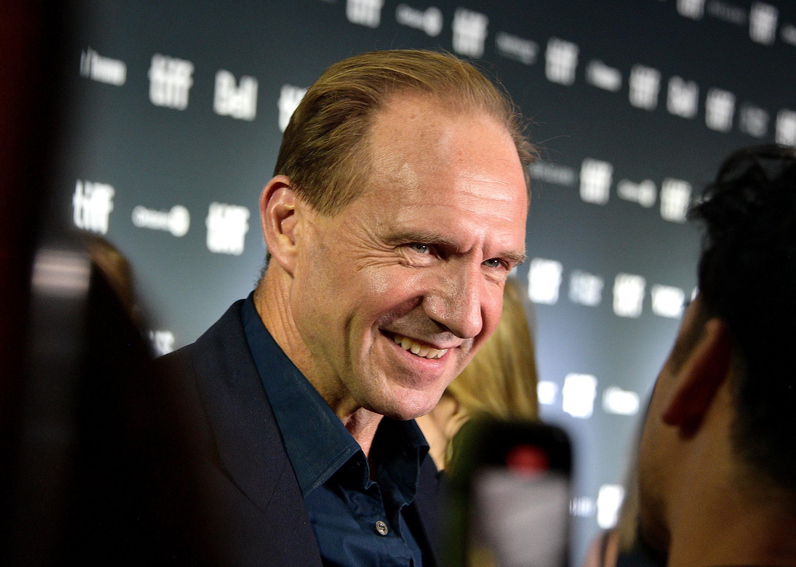Ralph Fiennes in a blue shirt and black jacket.