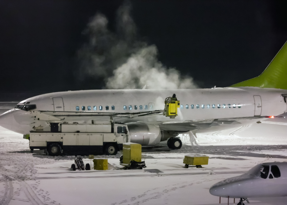 Service attendant on a lift de-ices a plane in snow at night.