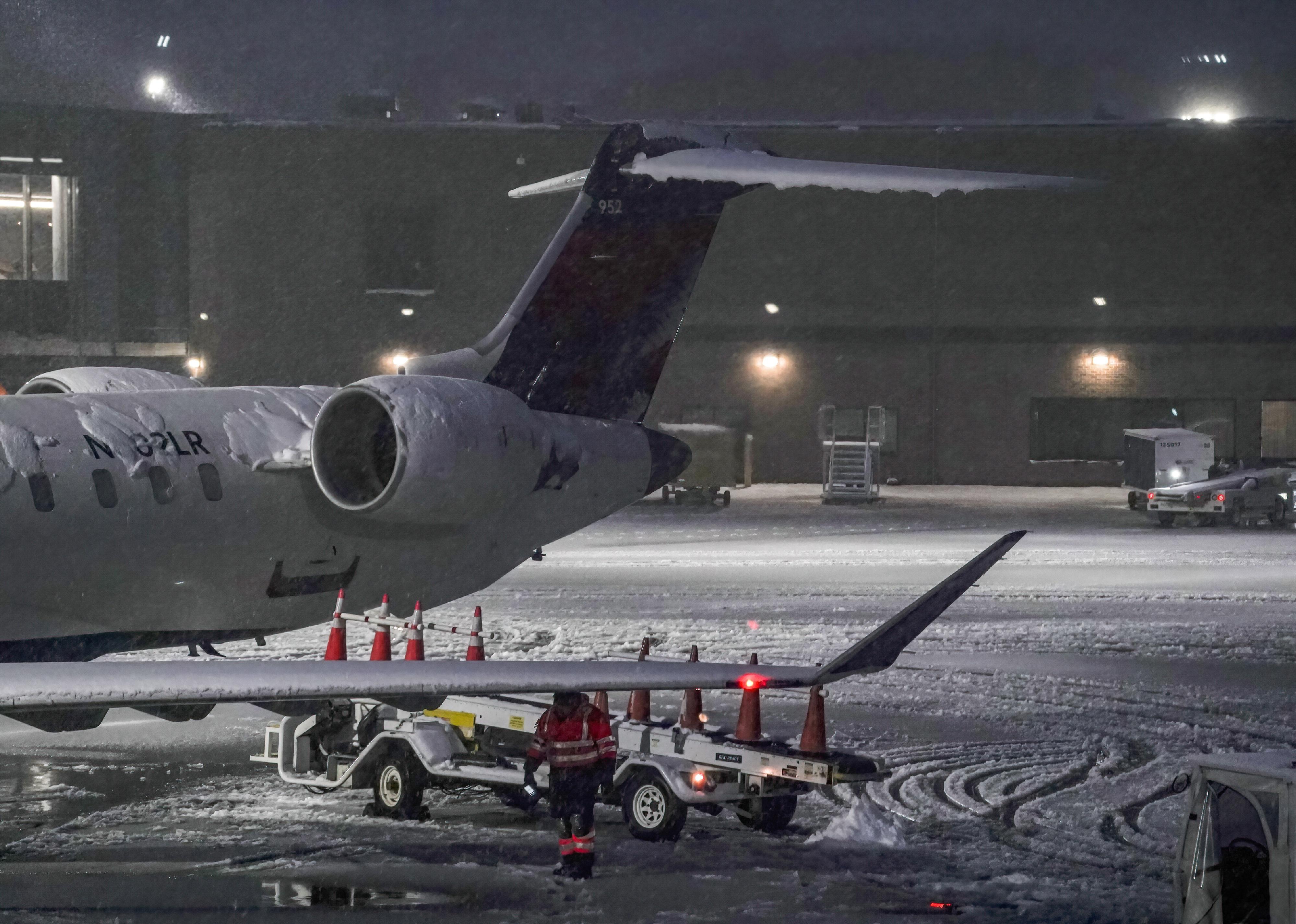 An airport employee working in a snowstorm next to an airplane.