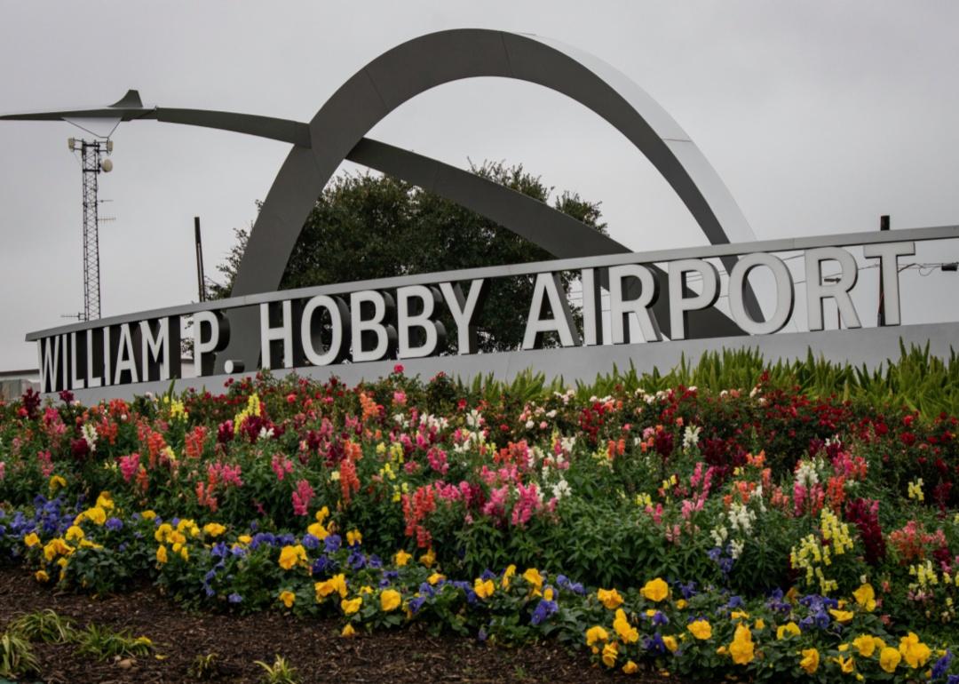 The William P. Hobby airport sign and metal arches in front of a blooming flower bed.