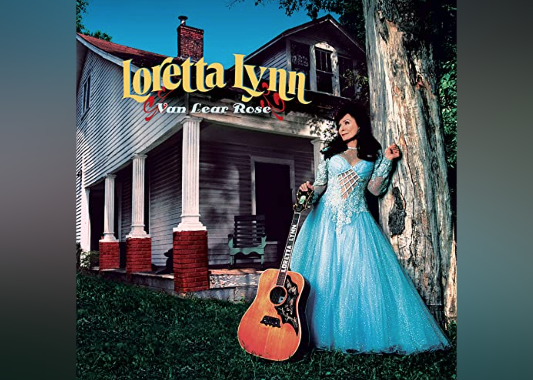 Loretta Lynn in a blue gown leaning on a tree in front of a house with a guitar leaning against her side.