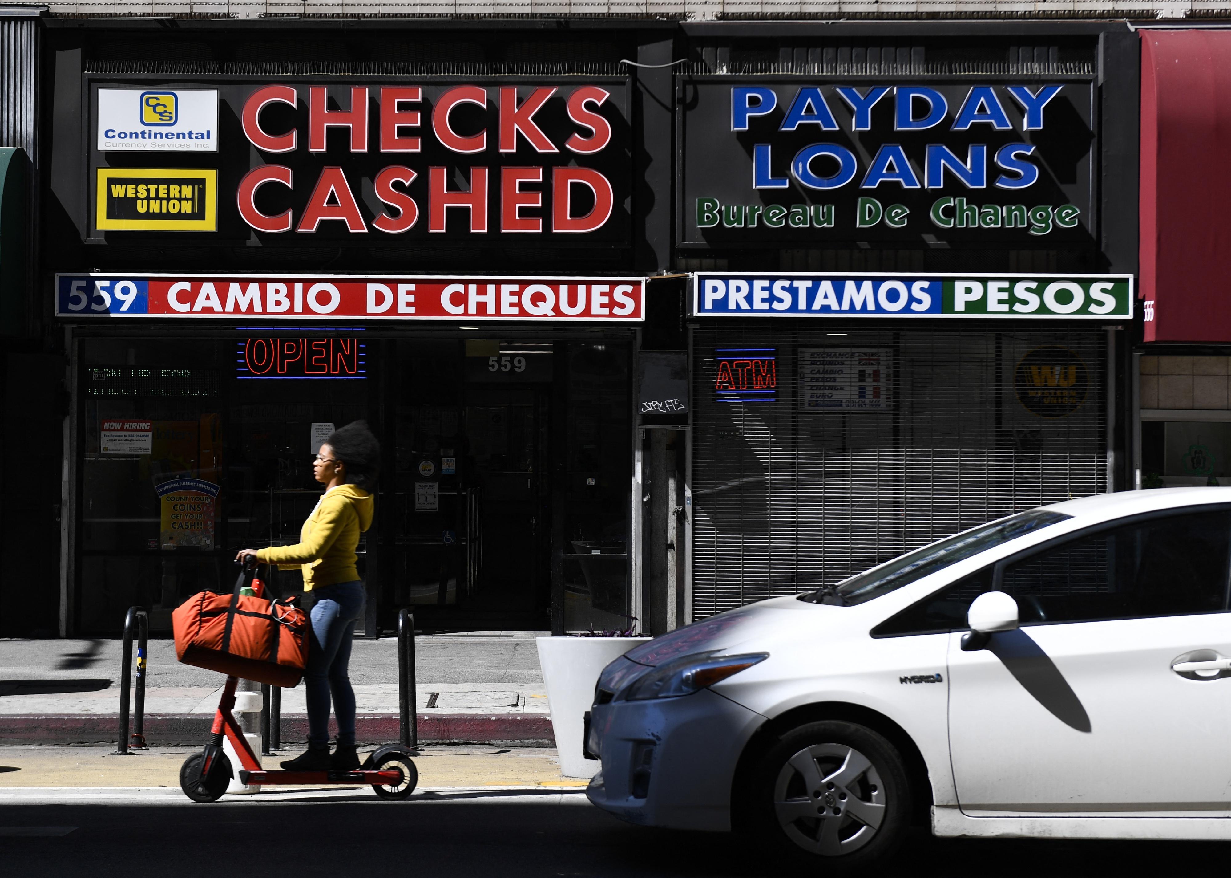A woman rides a scooter past a payday loan store.