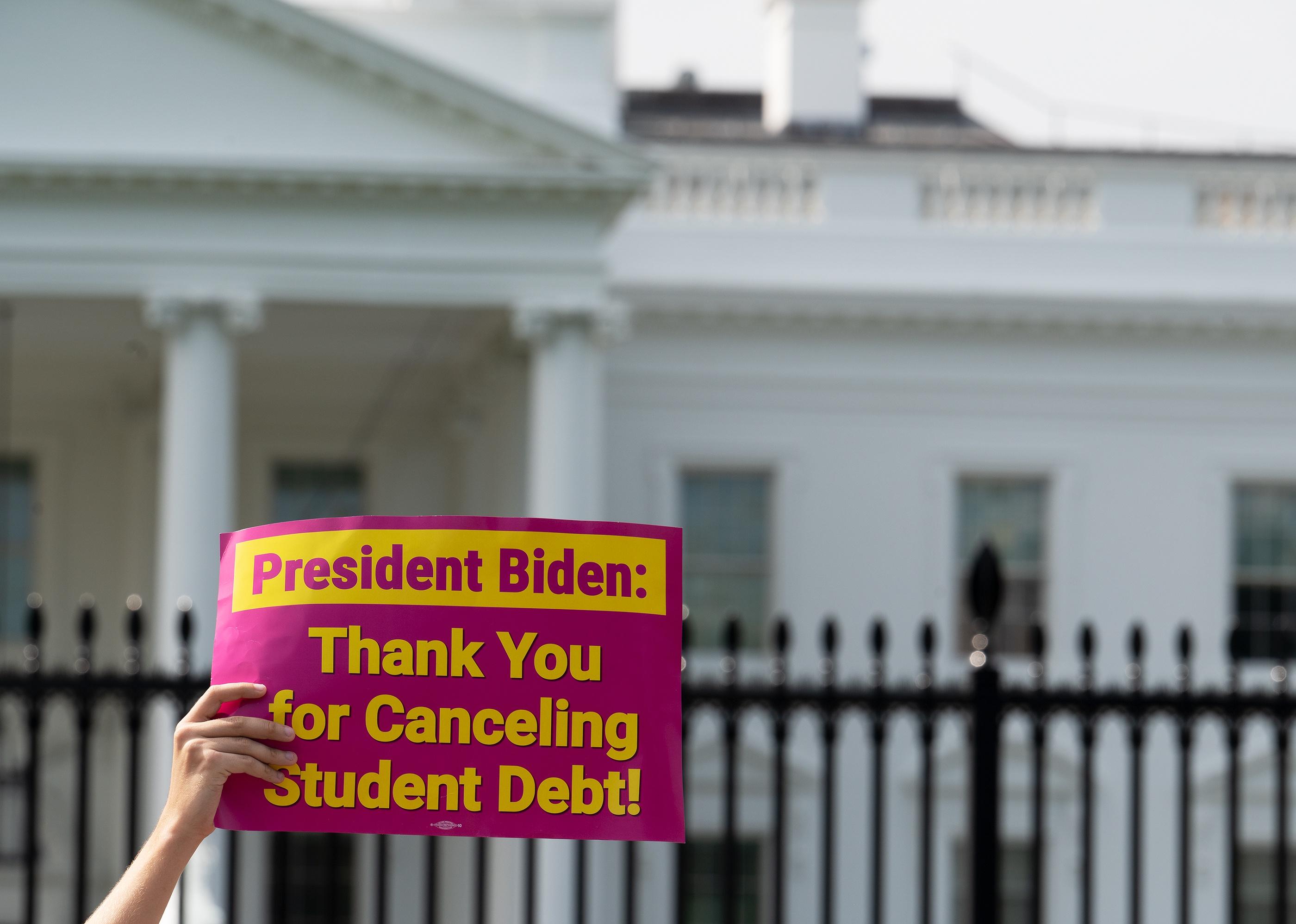 A person holds up a pink sign thanking President Biden for canceling student debt.