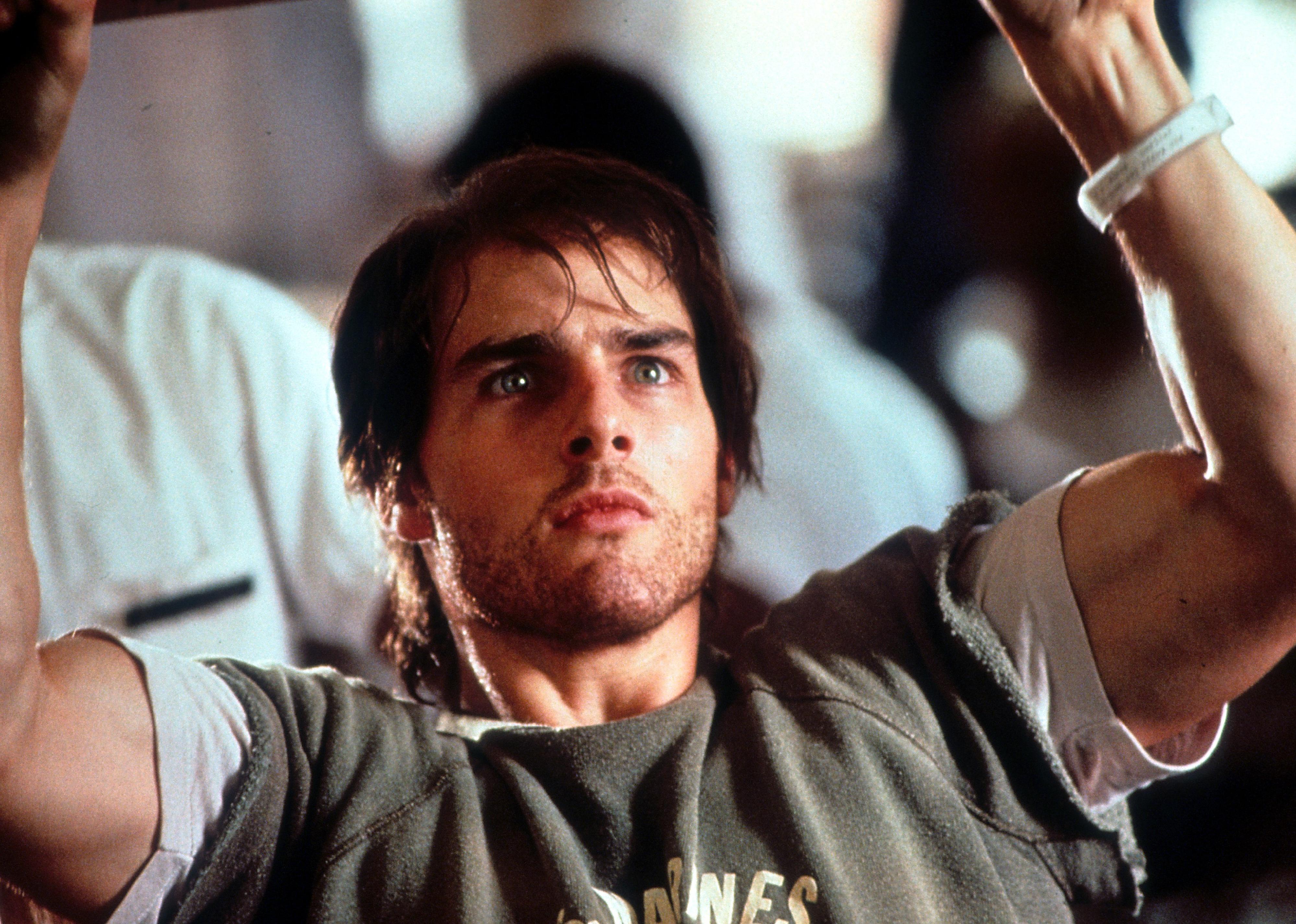 Tom Cruise in a Marines cut off sweatshirt doing chin ups.