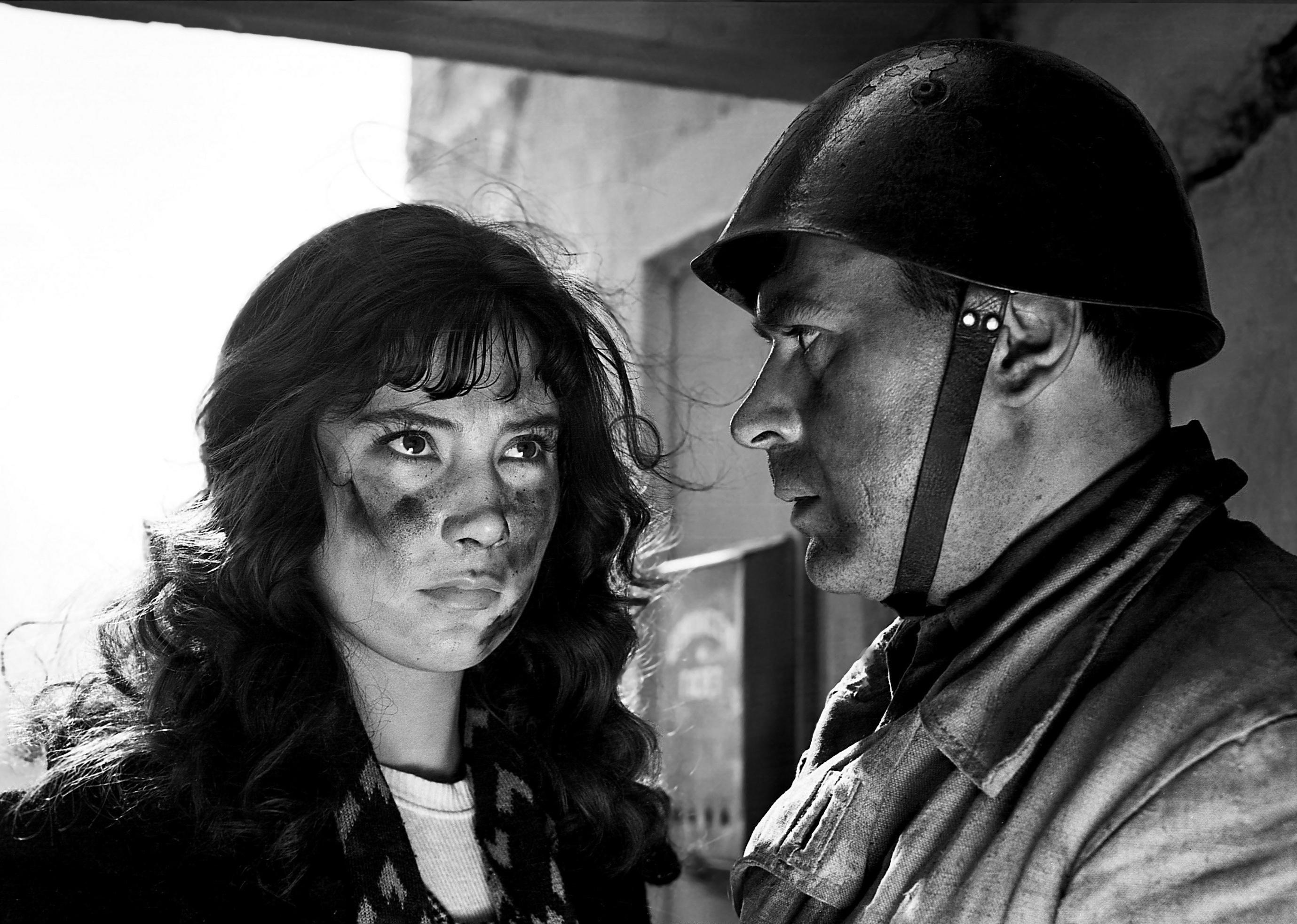A woman with a dirty face next to a man in a military uniform and helmet.