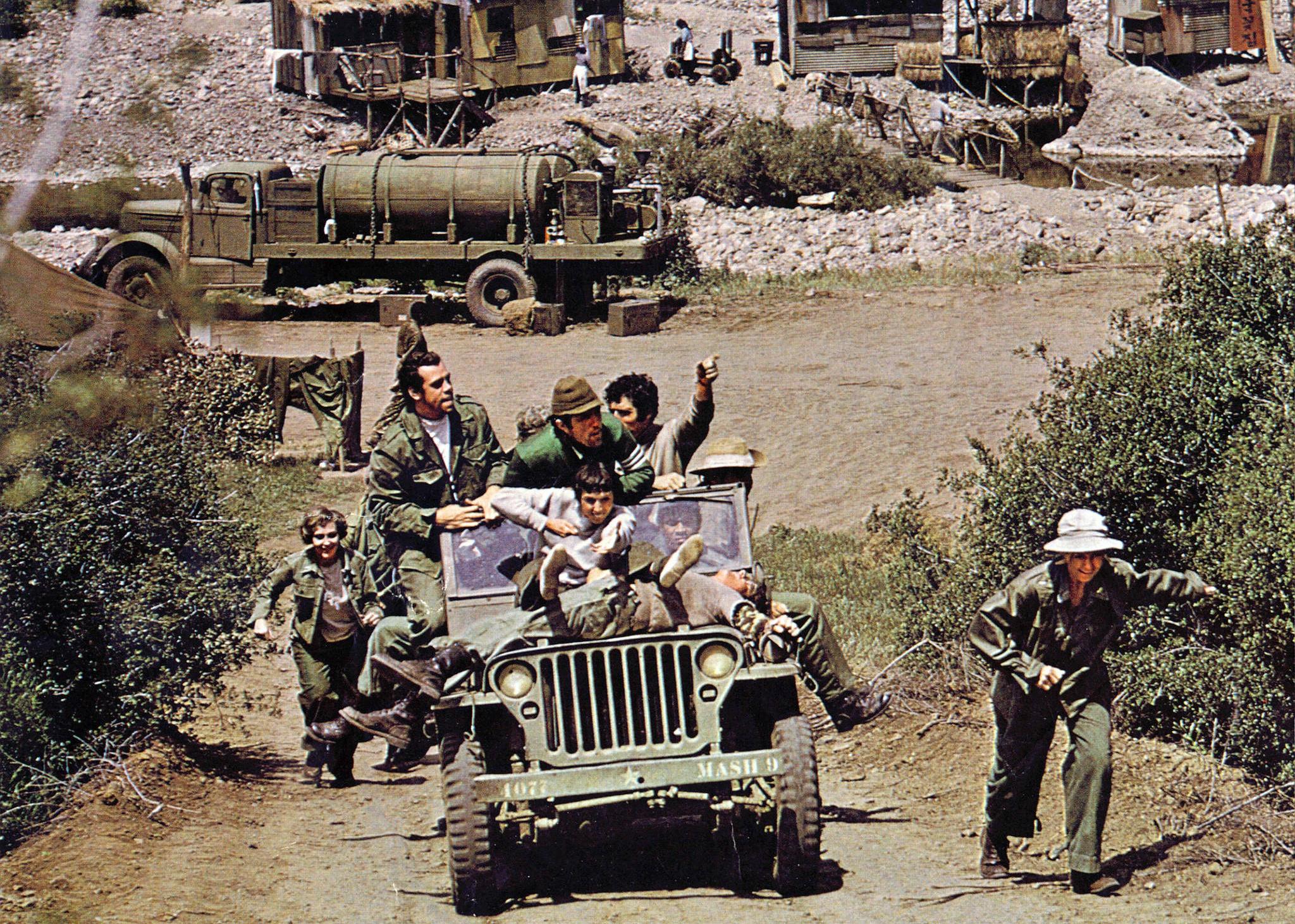 Military members piled into and running with an army jeep uphill.