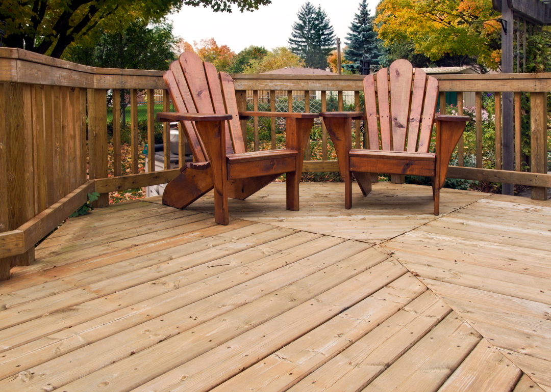 A wood deck with two adirondack chairs and a railing.