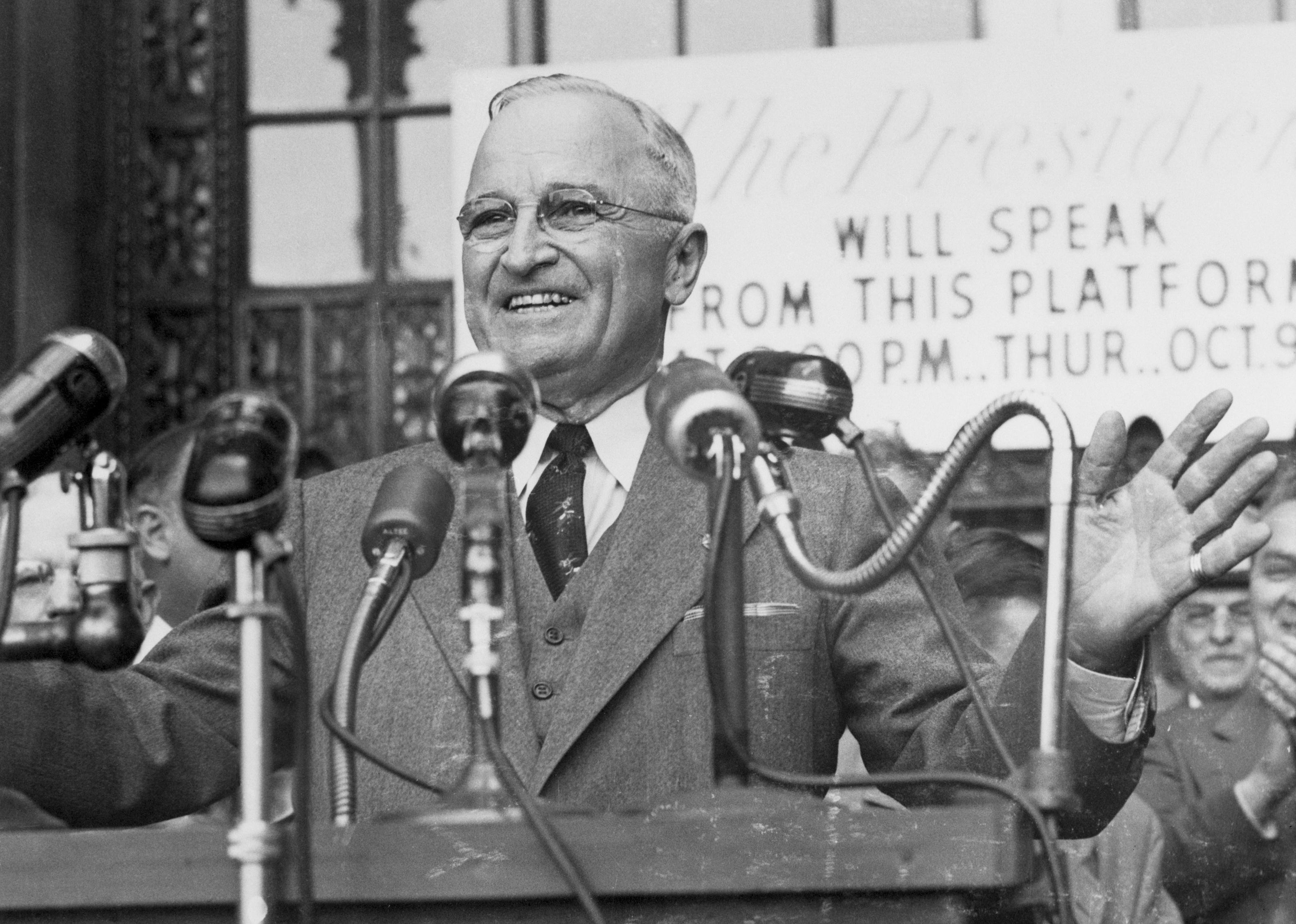 Harry S. Truman speaking at a podium full of microphones.