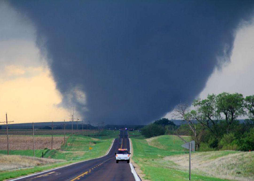 A white pickup truck driving toward a massive tornado in a rural area.