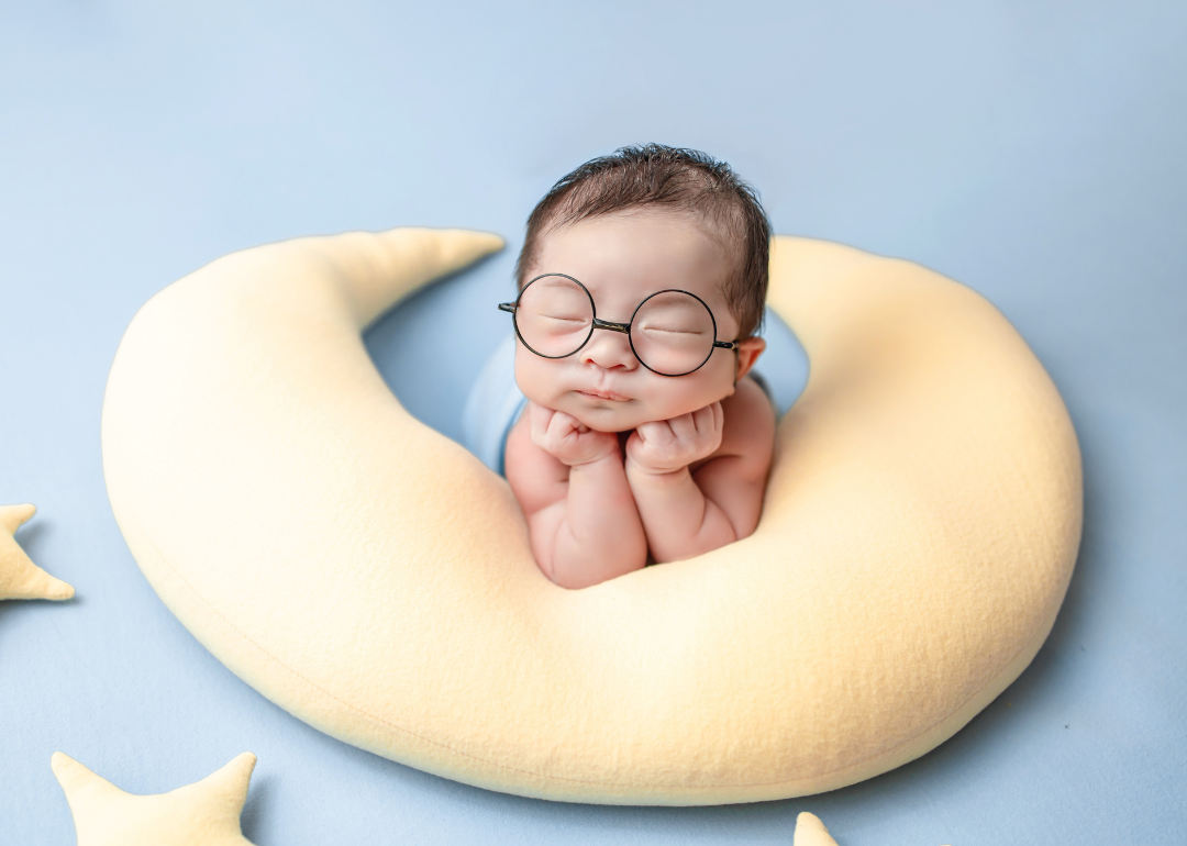 A baby wearing glasses asleep on a yellow moon pillow.