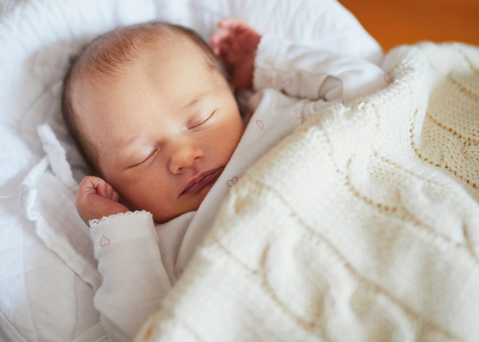 A sleeping baby under a white knitted blanket.