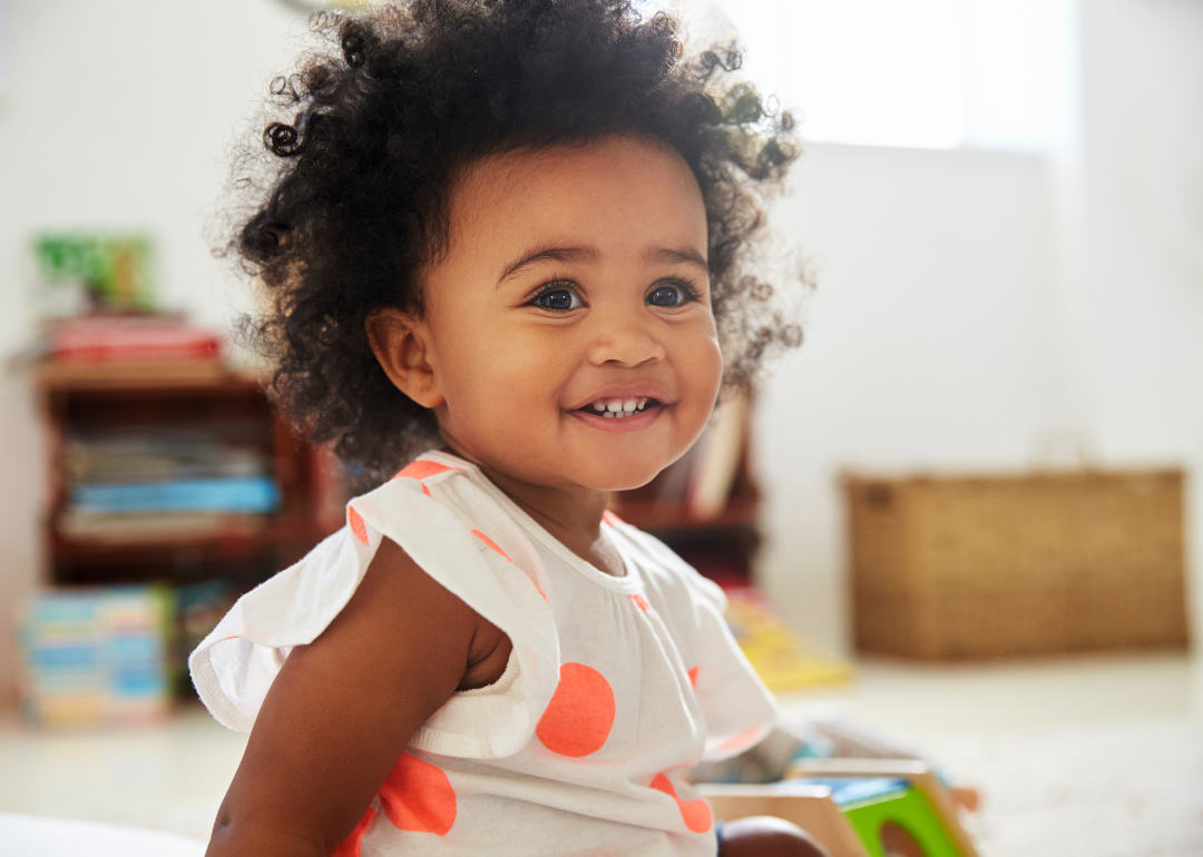 A smiling baby in an orange and white polka dot outfit.