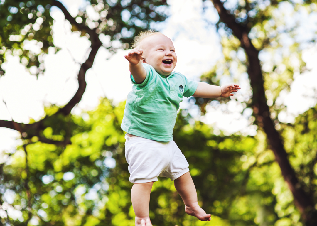 A baby up in the air wearing a green shirt and white shorts.