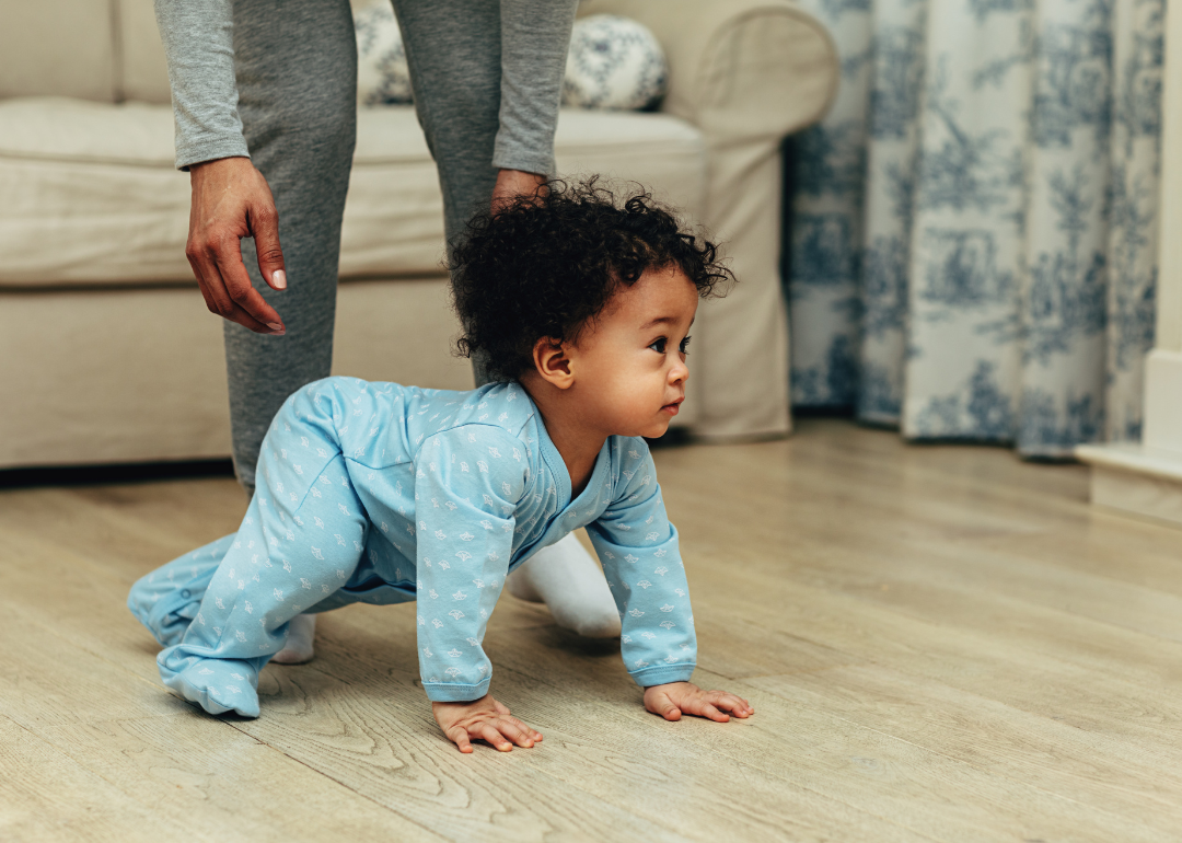 A baby in a blue onesie crawling.