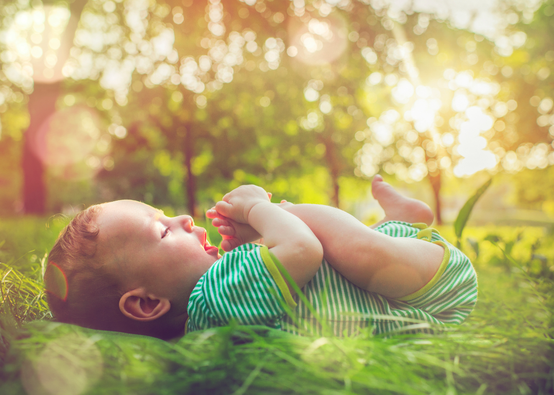A baby boy in a green outfit lying on the grass outside.