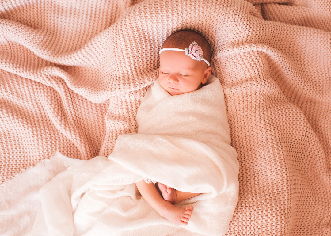 A sleeping baby girl wrapped in a white swaddle on a pink blanket.