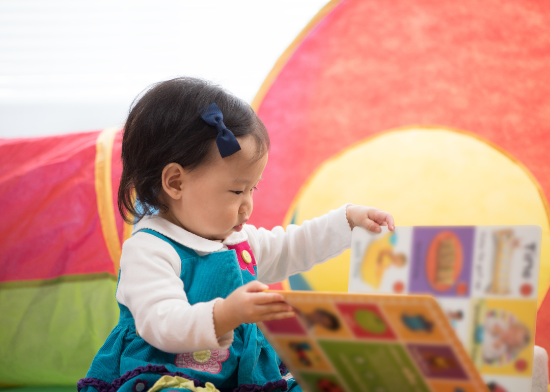 A baby girl in a blue dress holding a book.