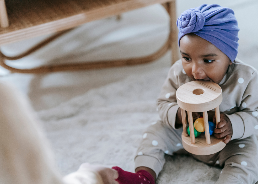 A baby girl in a tan outfit with a purple head wrap.