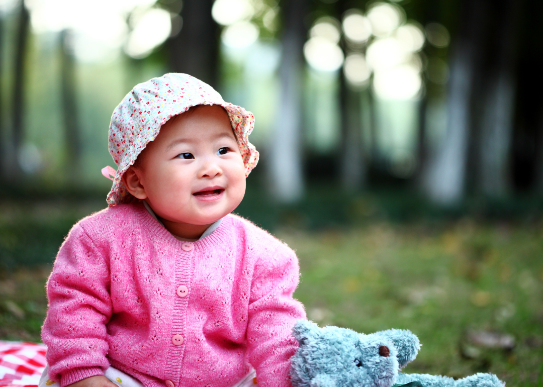 A baby girl in a pink cardigan and floral hat outside.