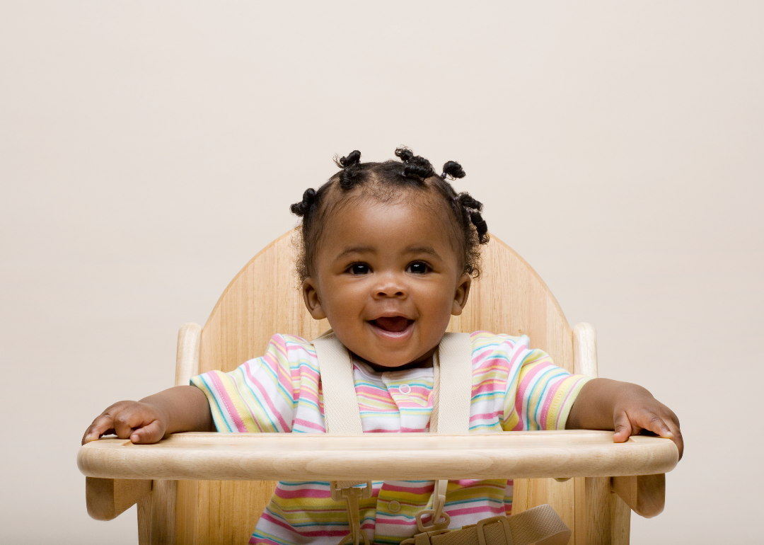 A smiling baby girl in a high chair wearing a striped shirt.