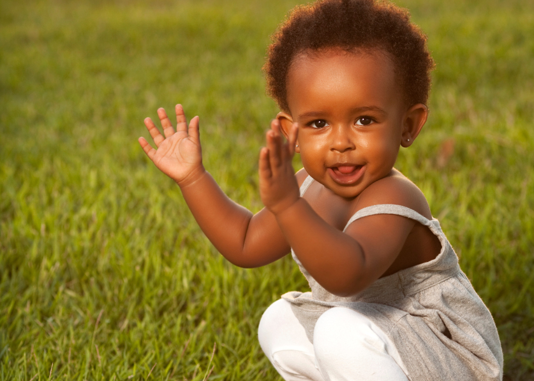 A baby girl clapping in the grass.