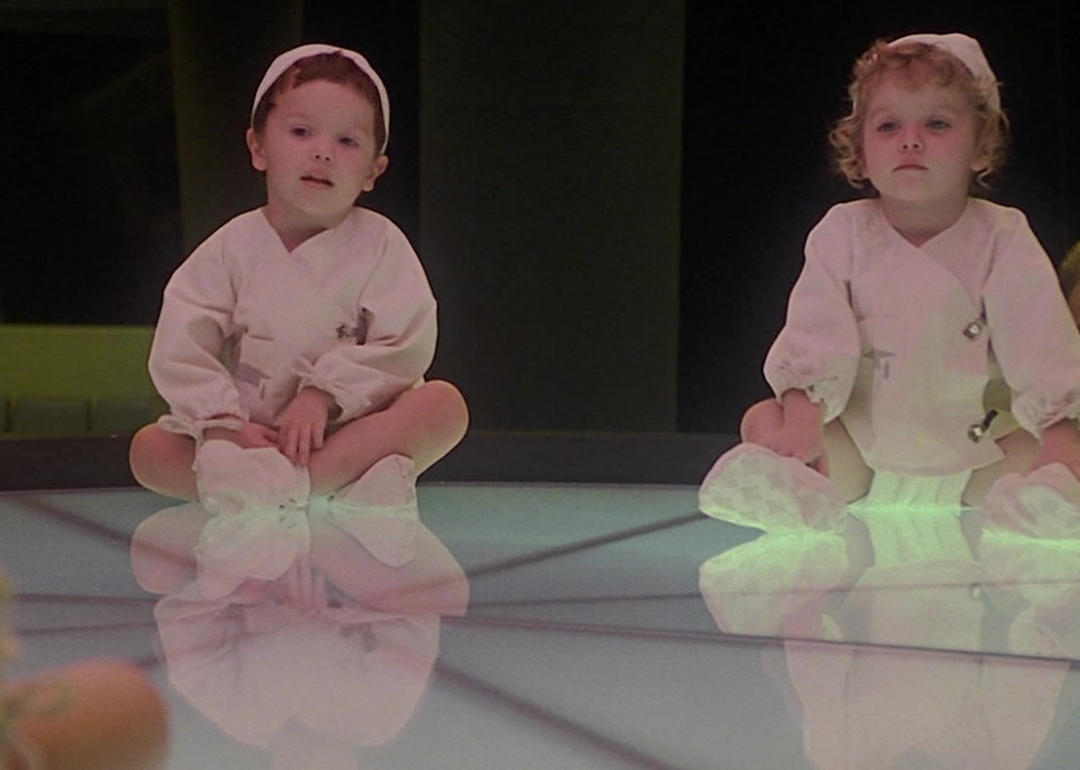 Babies dressed in all white sitting on a lit up platform.