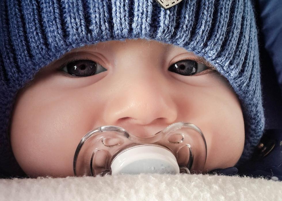 A close-up of a baby with a blue hat and a pacifier.