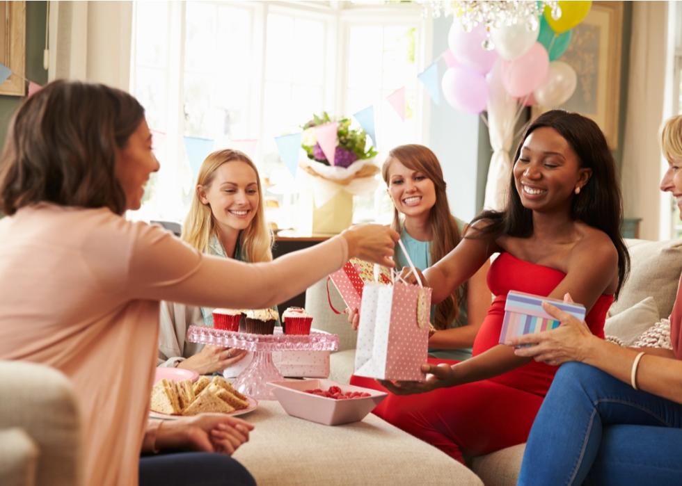 Women sitting on a couch opening baby shower gifts.