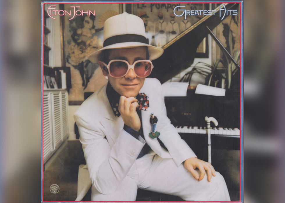 Elton John in a white suit and hat in front of a piano.