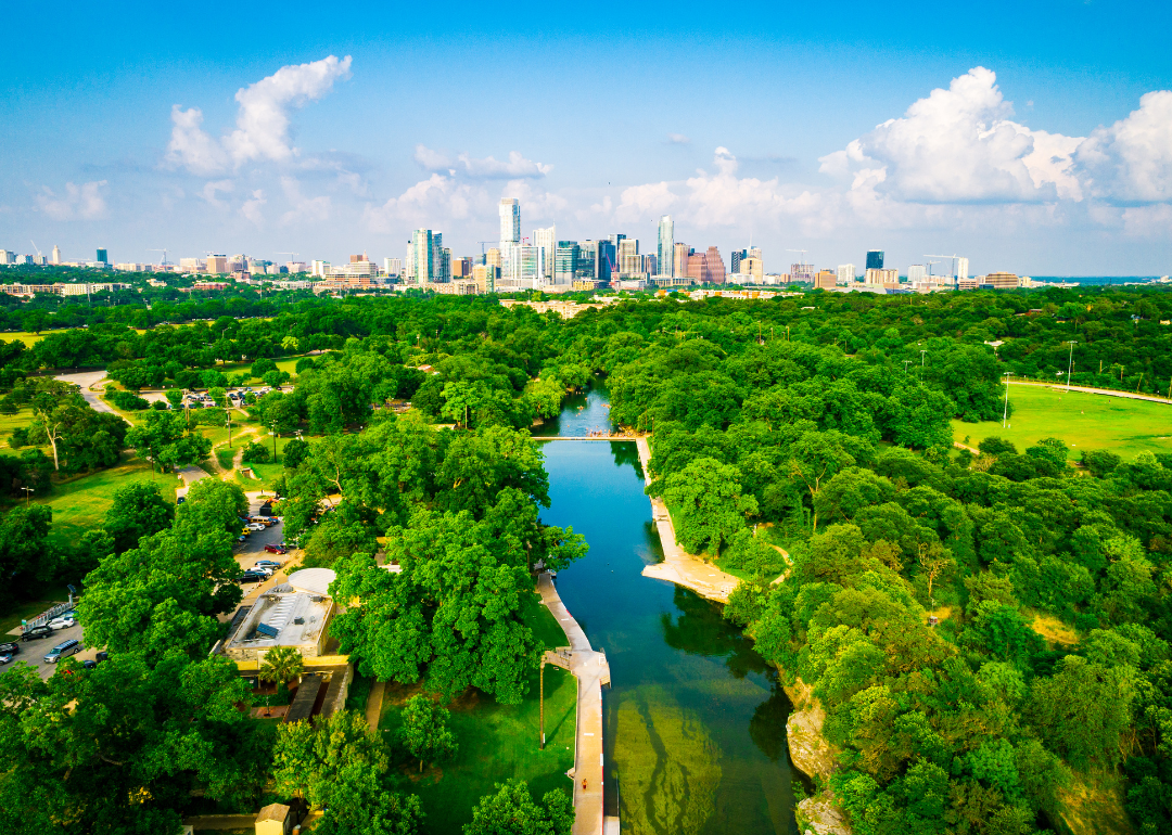 An aerial view of green trees and water with downtown Austin in the background.